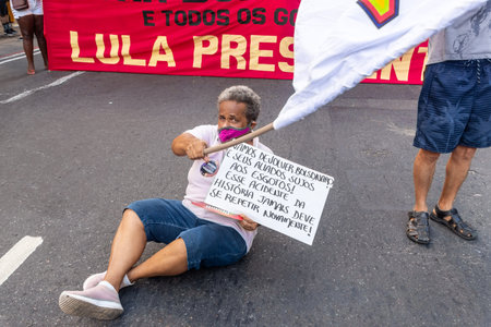 Salvador, Bahia, Brazil - April 09, 2022: Militant protesting against the far-right presidential candidate Jair Bolsonaro, with a flag and a poster calling for the resignation of the presidency.のeditorial素材