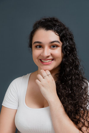 Young smiling woman looking at camera with hand on chin. Against gray background.