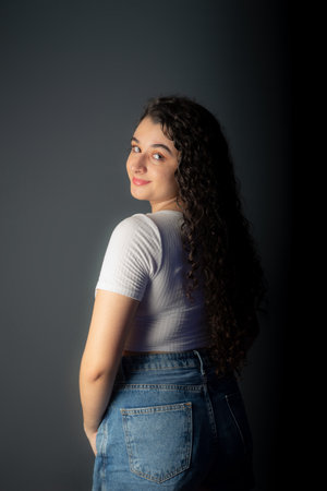 Profile of beautiful young woman with black hair wearing white shirt and looking at camera. Against gray background.の写真素材