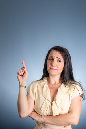 Young business woman, cheerful, pointing right finger up. Isolated against light blue background.の写真素材