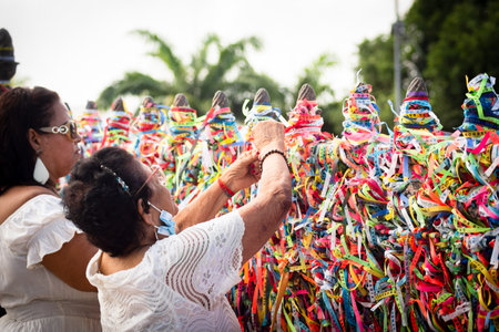 Salvador, Bahia, Brazil - January 06, 2023: A Catholic woman places a ribbon on the iron railing of Senhor do Bonfim church during an open air mass in Salvador, Bahia.のeditorial素材