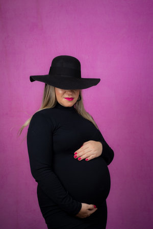 Pregnant woman in hat holding barria with hands. Isolated against pink background.