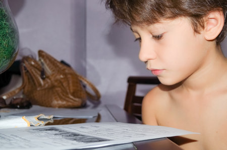 Boy, shirtless student, sitting at home, reading homework pages. Education concept.の写真素材