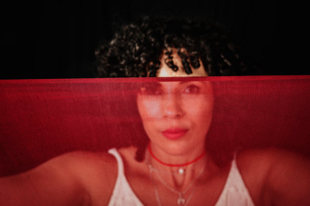 Portrait of a woman with red cloth stretched in front of her face. isolated on black background.の写真素材