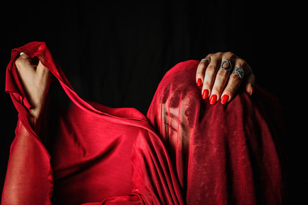 Beautiful woman with red cloth over her head making hand gestures. Isolated on black background.の写真素材