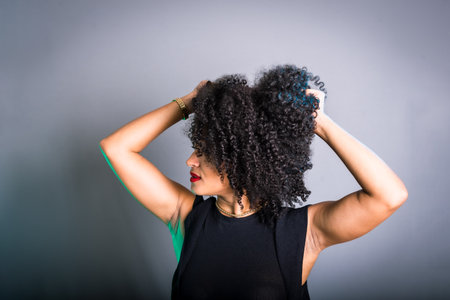 Portrait of beautiful young brunette woman messing with her hair. Dressed in black. Isolated on gray backgroundの写真素材