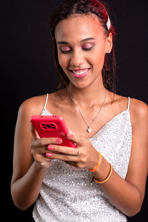 Portrait of smiling teenager looking and using cell phone. Isolated on black background.の写真素材