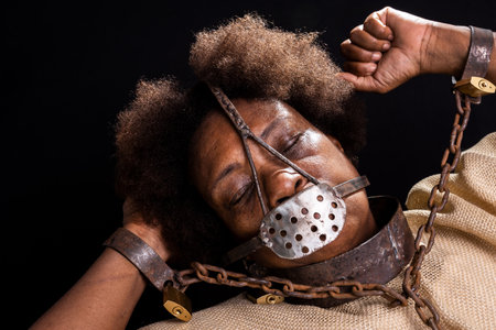 Portrait of a black woman in chains with an iron mask on her face representing the slave Anastacia. Slavery in Brazil. Isolated on black background.の写真素材
