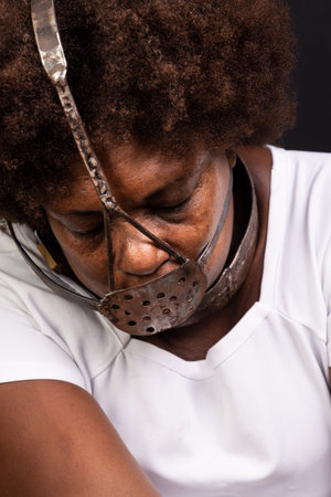Black woman in chains with an iron mask on her face, representing the slave Anastacia. Pain and suffering, torture. Against black background.の写真素材