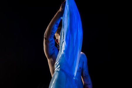 Young man moves a blue bag over his head. No shirt. Isolated on black background.の写真素材