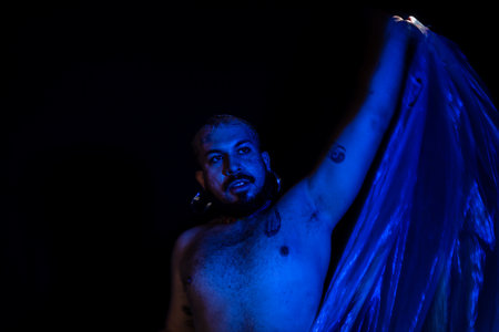 Young man moves a blue bag over his head. No shirt. Isolated on black background.の写真素材