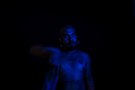 Young man moves a blue bag over his head. No shirt. Isolated on black background.