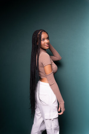 Beautiful young woman, standing, messing with her long hair. Isolated on dark cyan background.の写真素材