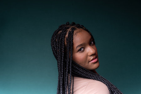 Beautiful, happy and confident young woman with braided hair. Isolated on dark cyan background.の写真素材