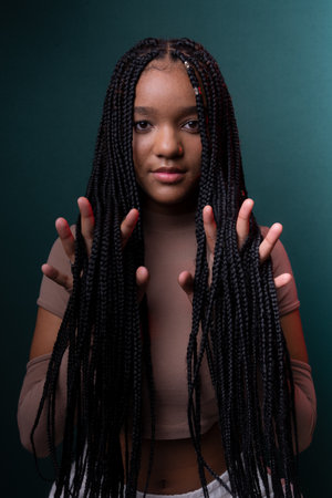 Young pretty black woman showing her hands through her braided hair. Isolated on dark cyan background.の写真素材