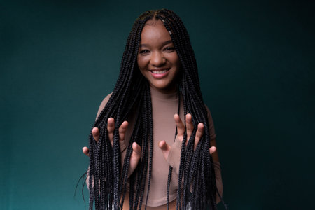 Young pretty black woman showing her hands through her braided hair. Isolated on dark cyan background.の写真素材