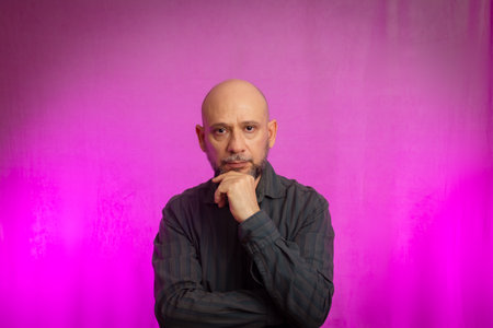 Portrait of a serious 50-year-old man with a beard and bald head. Isolated on pink background.の写真素材