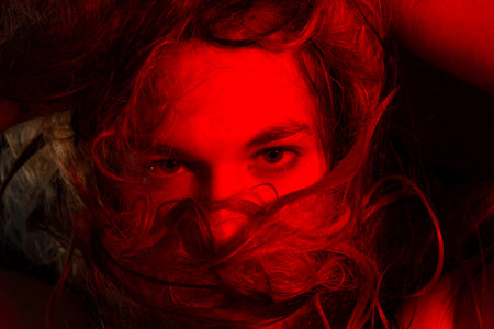 Close-up portrait of handsome young man with hair all over his face. Studio red filter. isolated on dark background.の写真素材