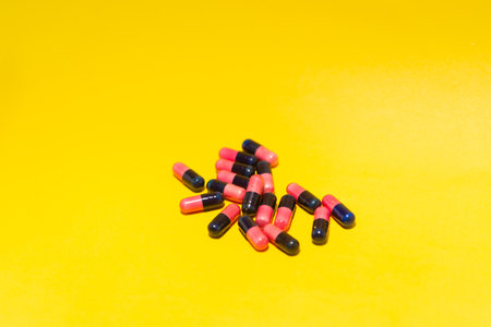 Several pills of red and black color arranged on top of a yellow surface. Medical supplies.
