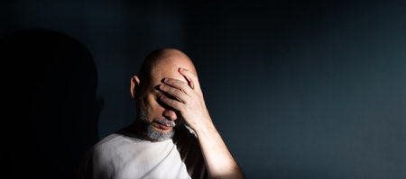 Sad man suffering from headache or migraine. Stressed guy with painful facial expression feeling terrible weakness or depression. Isolated on dark background.の写真素材
