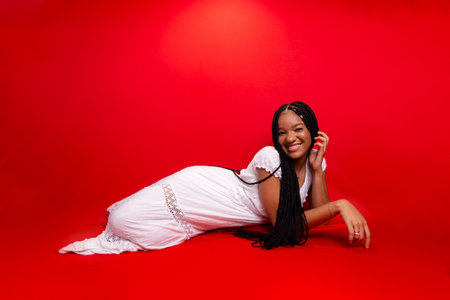 Beautiful young black woman sitting down smiling at the camera. Isolated on red backgroundの写真素材