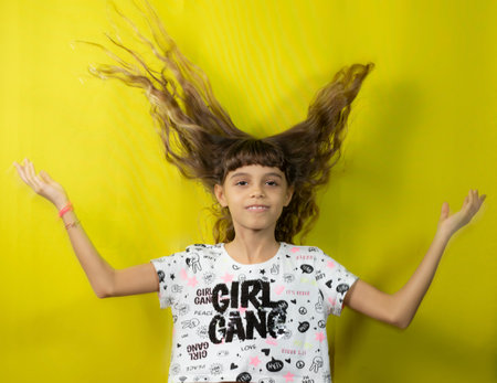 Beautiful girl throwing her long hair up. Isolated on yellow background.の写真素材