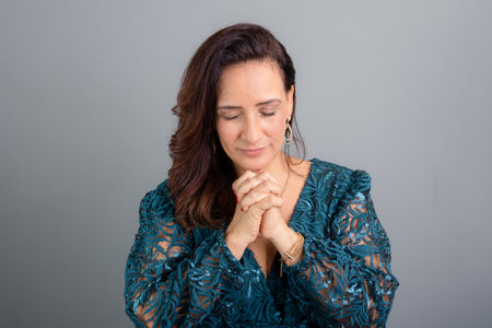 Studio portrait beautiful mature woman with praying hands. Concentrated and hopeful person. Isolated on gray background.の写真素材