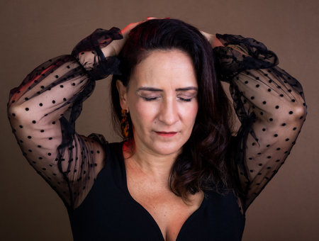 Coaching woman in black clothing with hands on the back of her head in a sign of concern. Isolated on brown background.の写真素材