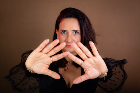 Coaching, beautiful woman in black clothing making forward hand gestures. Communicative and democratic management. Isolated on brown background.の写真素材
