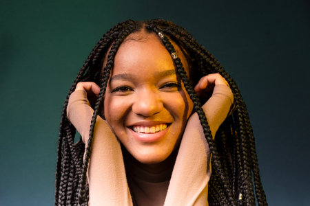 Portrait of a smiling young woman with pigtails, hands on her chin. Isolated on dark cyan...