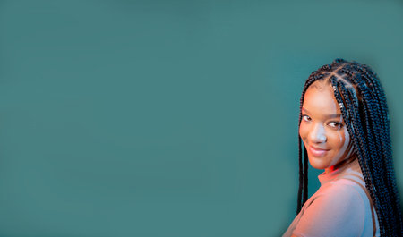 Studio portrait of beautiful young woman with braids in her hair looking at camera. Isolated on dark cyan background.の写真素材