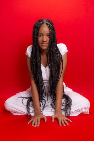 Brunette woman, young, sitting showing the long braids of her hair. Isolated on red backgroundの写真素材