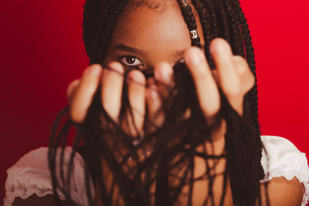 Close-up portrait of black woman with holding her braids to her face. Isolated on red background