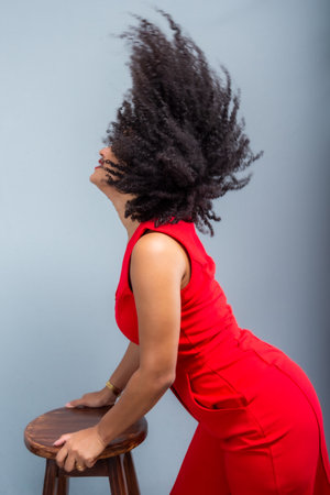 Beautiful woman, standing, wearing red outfit playing with her curly hair. Isolated on light gray...
