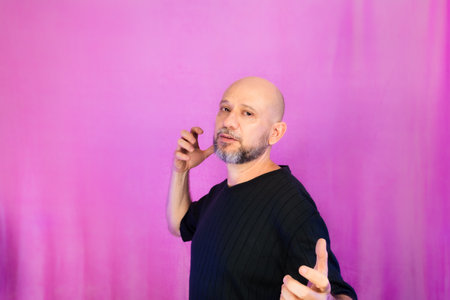 Bearded and bald man making various signs with his hands. Isolated on pink background.