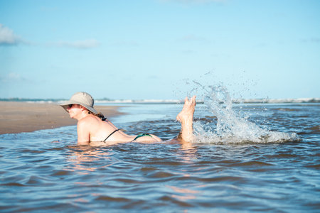 Woman in bikini and hat relaxing and playing by the sea. Taquari, Guaibim beach, Valenca, Bahia.の写真素材