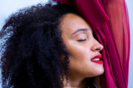 Studio portrait of a young woman, with curly hair, manipulating a lilac cloth. Isolated on light gray background.の写真素材