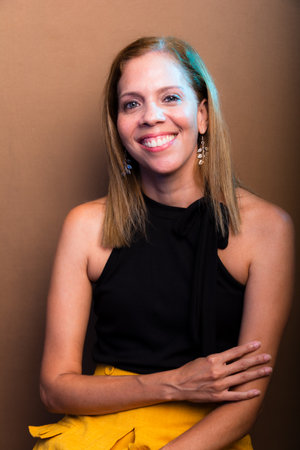 Portrait of smiling, happy woman wearing black and yellow, isolated on brown background.