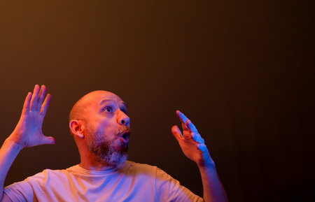 Happy bald bearded man making funny hand gestures. Concept of strength, achievement and success. Isolated on dark red background.の写真素材