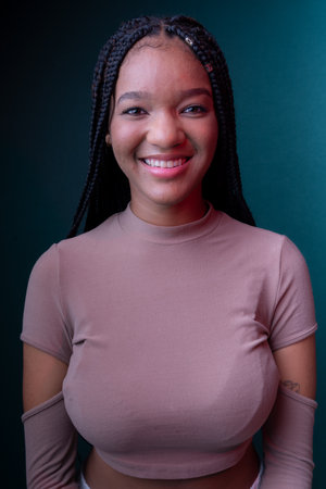 Beautiful young woman with braids, smiling. Isolated on dark cyan background.の写真素材