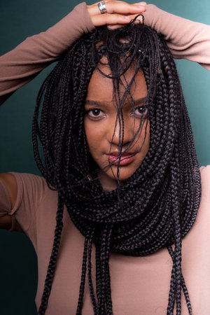 Close-up portrait of a beautiful young black woman with braided hair. Isolated on dark cyan background.の写真素材