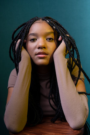 Portrait of a beautiful young woman with pigtails, hands on her chin. Isolated on dark cyan...