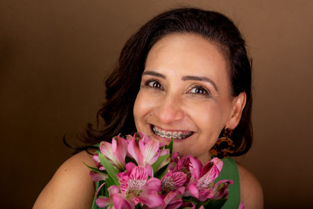 Close-up portrait of beautiful Caucasian woman holding bouquet of flowers close to her face. Passionate, happy person. Isolated on brown background.の写真素材