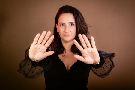 Coaching, beautiful woman in black clothing making forward hand gestures. Communicative and democratic management. Isolated on brown background.の写真素材