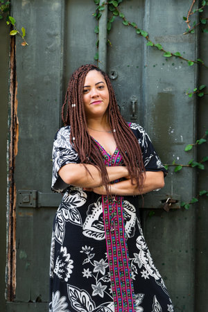 Portrait of a pretty woman with braids in her hair with her arms crossed against a green door with...