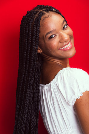 Beautiful young woman with long braids, confident and smiling. Isolated on red background.の写真素材