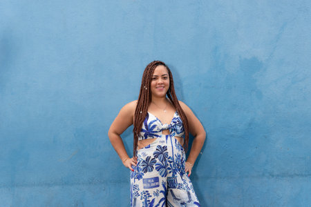Portrait of a beautiful woman standing with braids in her hair against a blue wall looking at the camera. Pelourinho, Brazil.の写真素材