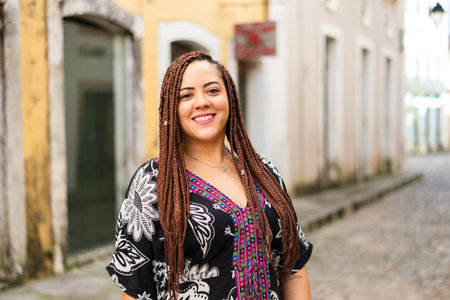 A woman crouched down on a cobbled street. Hair braids and African dress. Pelourinho, Brazil.の写真素材