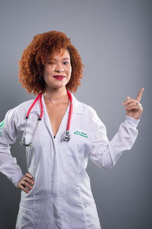 Veterinarian woman, pretty with red hair, showing a stethoscope to the camera in a white uniform. Isolated on gray background.の写真素材