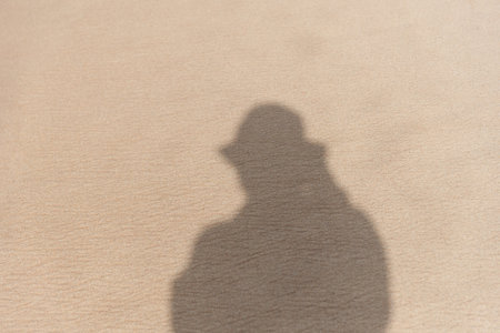 Shadow of a person wearing a hat on the sand of a beach. brown colored sandの写真素材